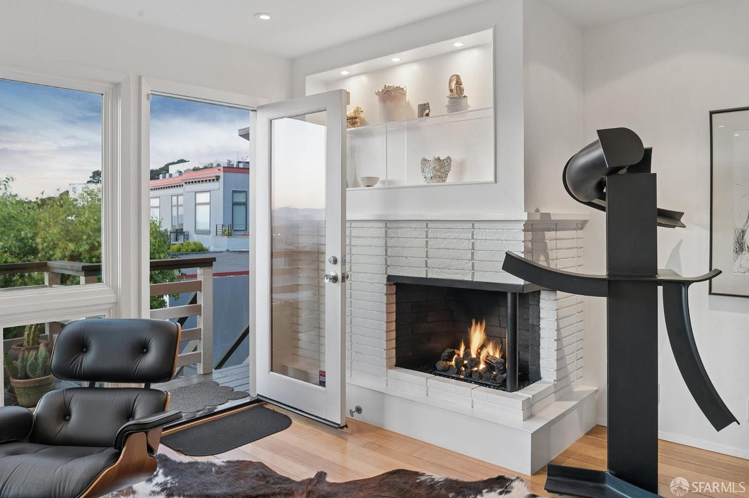 The lit white-brick corner fireplace at 138 Clifford Terrace, with built-in display shelves above and a wall of glass framing the northern view alongside
