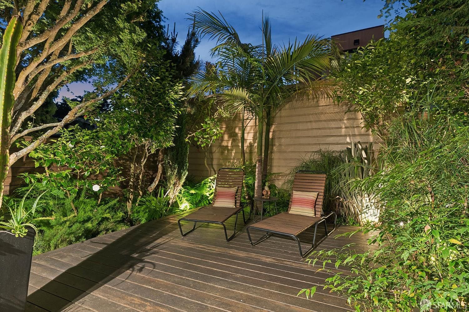 The landscaped garden at 138 Clifford Terrace at dusk, with lounge chairs, palms, and lit plantings on a wood deck