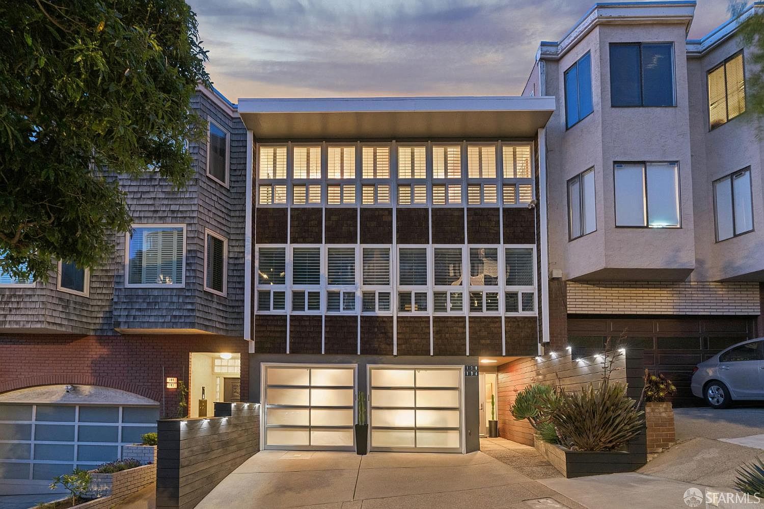 Twilight front elevation of 138 Clifford Terrace, a 1958 mid-century San Francisco condominium with an illuminated wall of windows above a two-bay garage